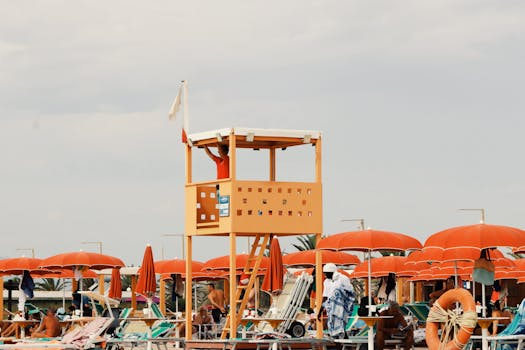 A lively beach scene in Sardegna, Italy with orange umbrellas and a lifeguard tower.